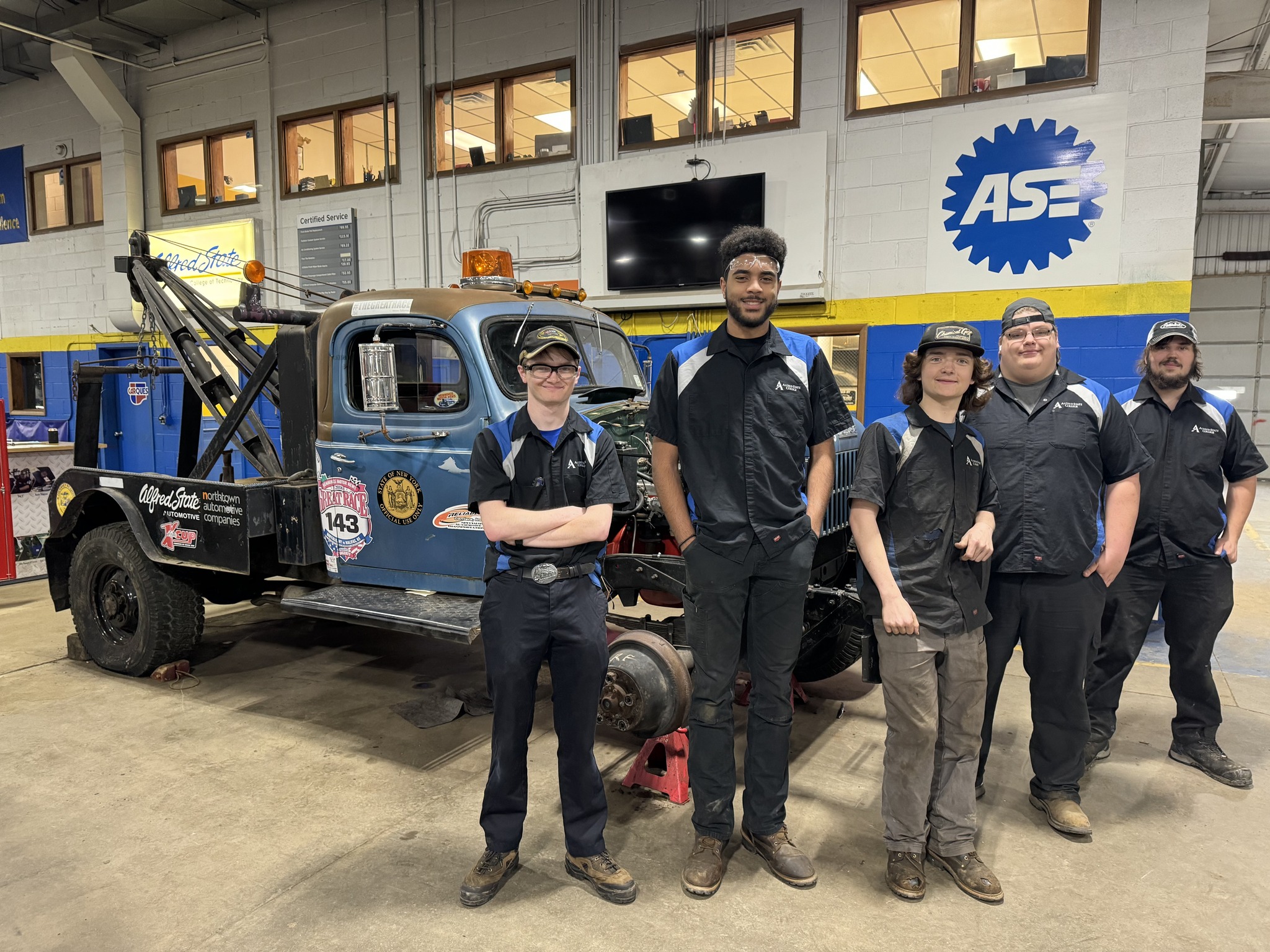 A group of five Western New York Works students stand in front of a tow truck they repaired for an automotive competition.