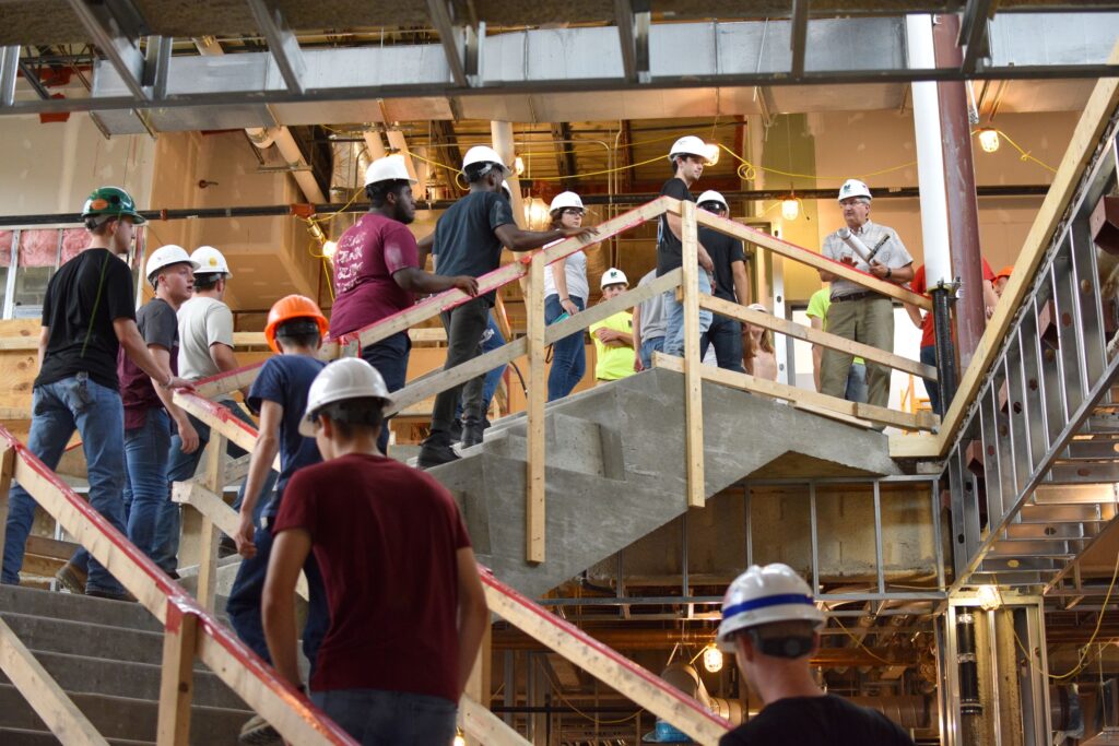 A group of students wearing hard hats follows an instructor for a construction career training class at a Western New York Works college.