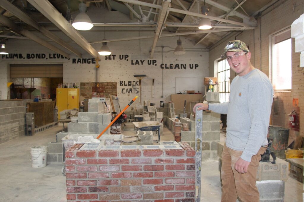 A male student wearing safety glasses stands by his brick work in a masonry class for a construction career training program at a Western New York Works college.