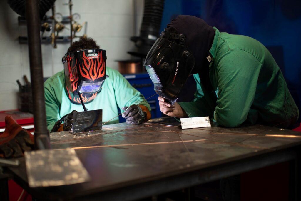 Two students wearing welding helmets practice working on metal in a class for a construction career training program at a Western New York Works college.