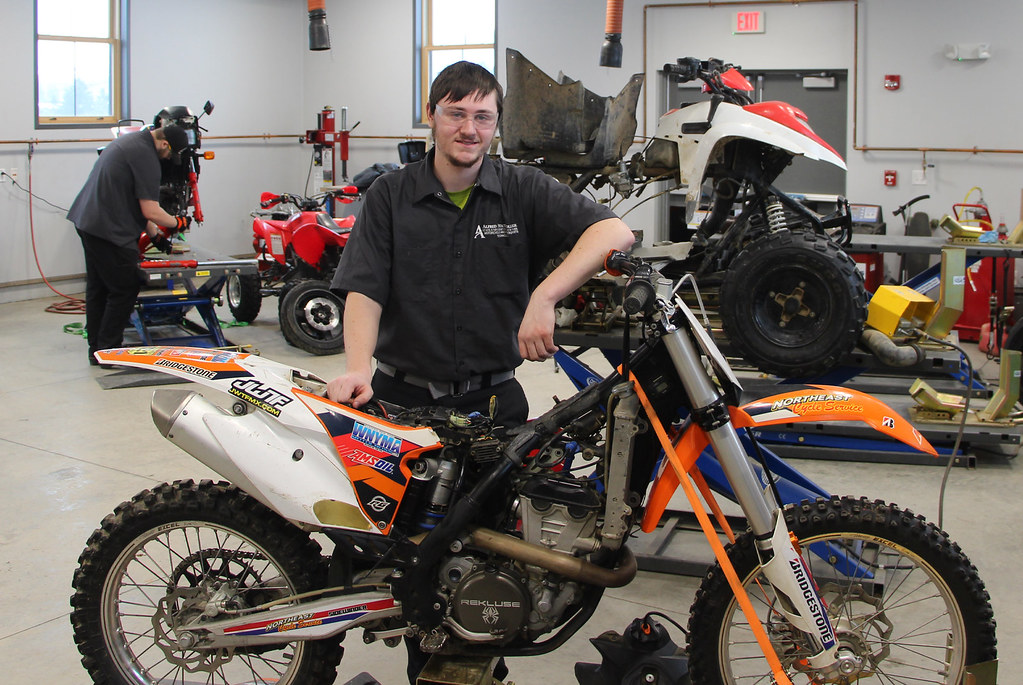 A student wearing safety glasses leans against a sport bike in a motorsports service technician class at a Western New York Works college.