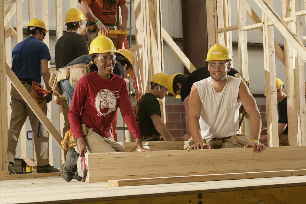 Students wearing hard hats and safety glasses work with wood beams in a carpentry class at a Western New York Works college.