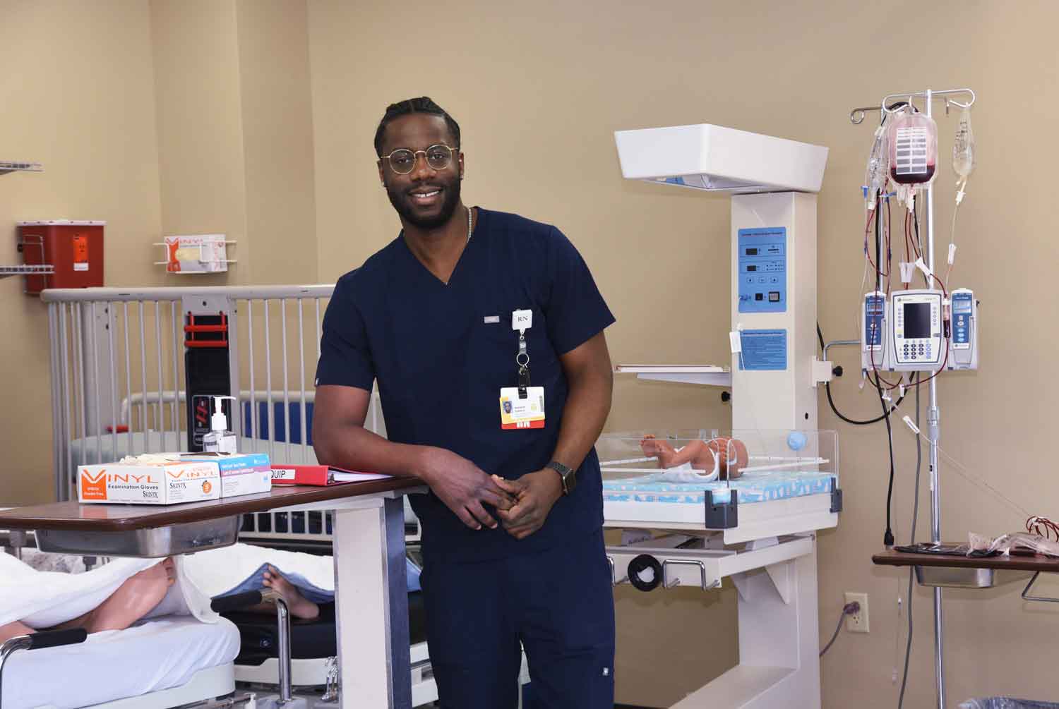 A nursing student wearing scrubs and a name tag stands in a simulated patient care space at a Western New York Works college.