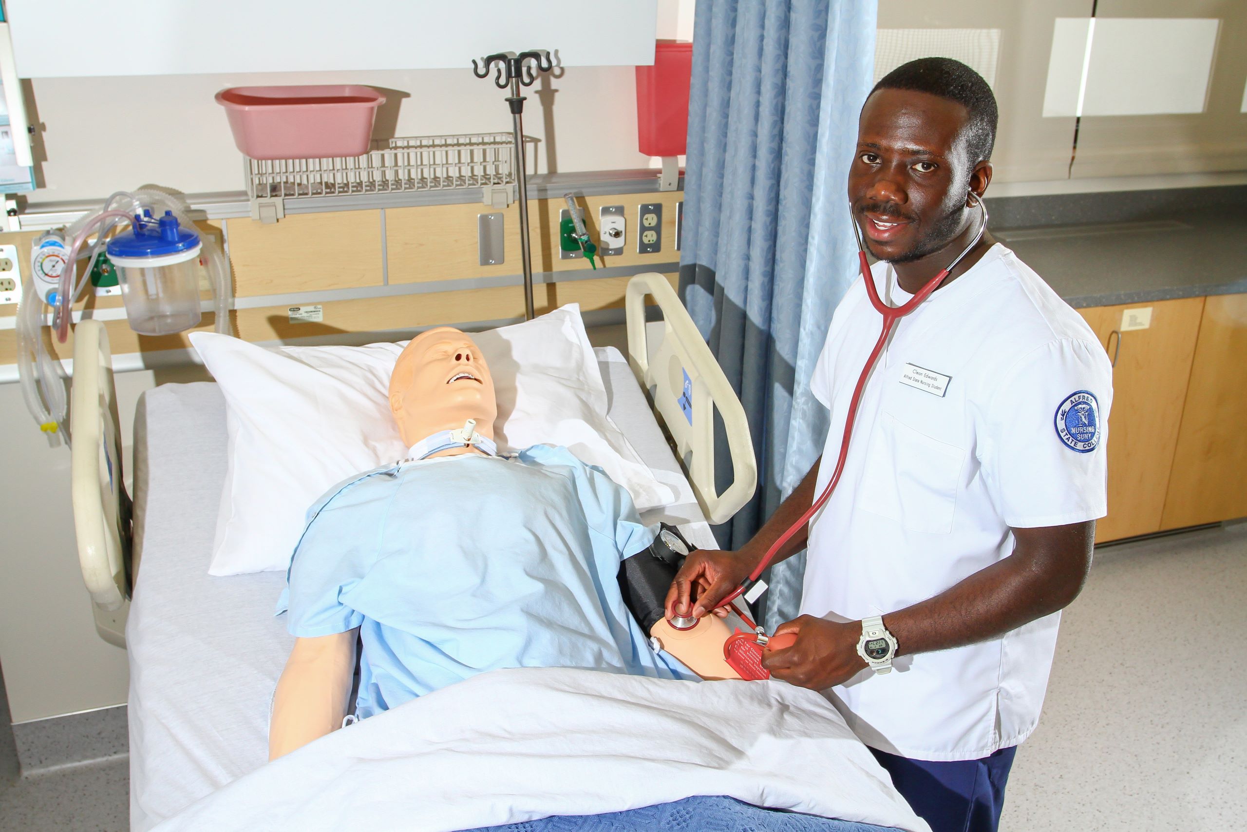 A male student in scrubs practices taking vitals on a simulated patient at a Western New York Works college.