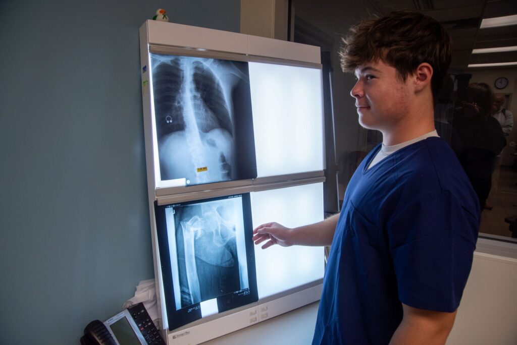 A male student in scrubs reviews imaging results in a class for a medical administrative and office assistant training program at a Western New York Works college