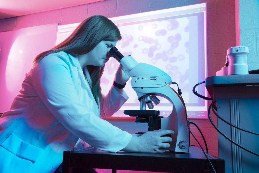 A student wearing a lab coat operates a microscope in a public health class at a Western New York Works college.