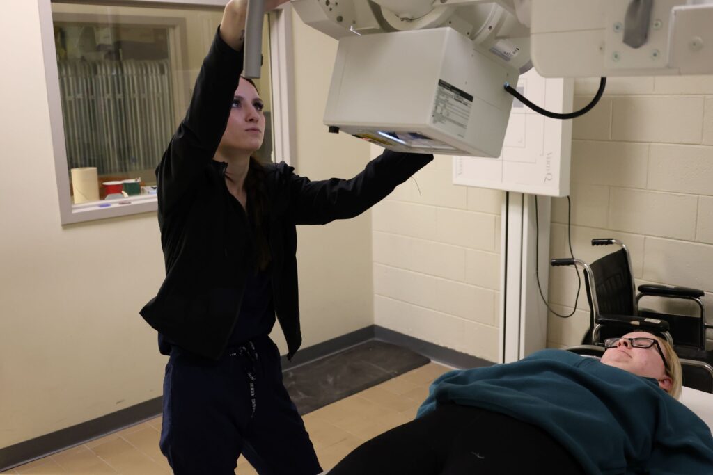 A radiology technologist student practices operating imaging equipment in a training space at a Western New York Works college