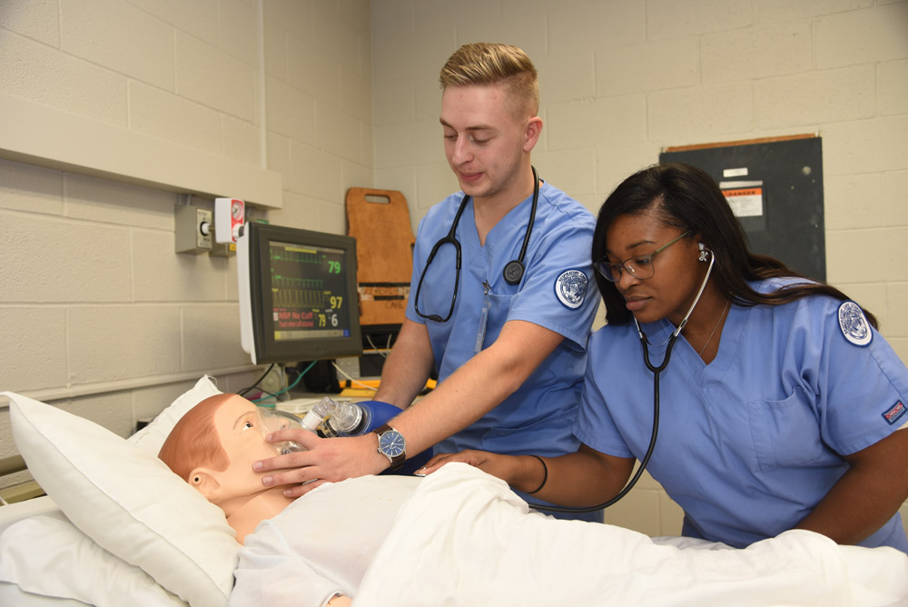 Two respiratory therapy students, one male and one female, practice monitoring patient breathing in a simulated environment at a Western New York Works college.