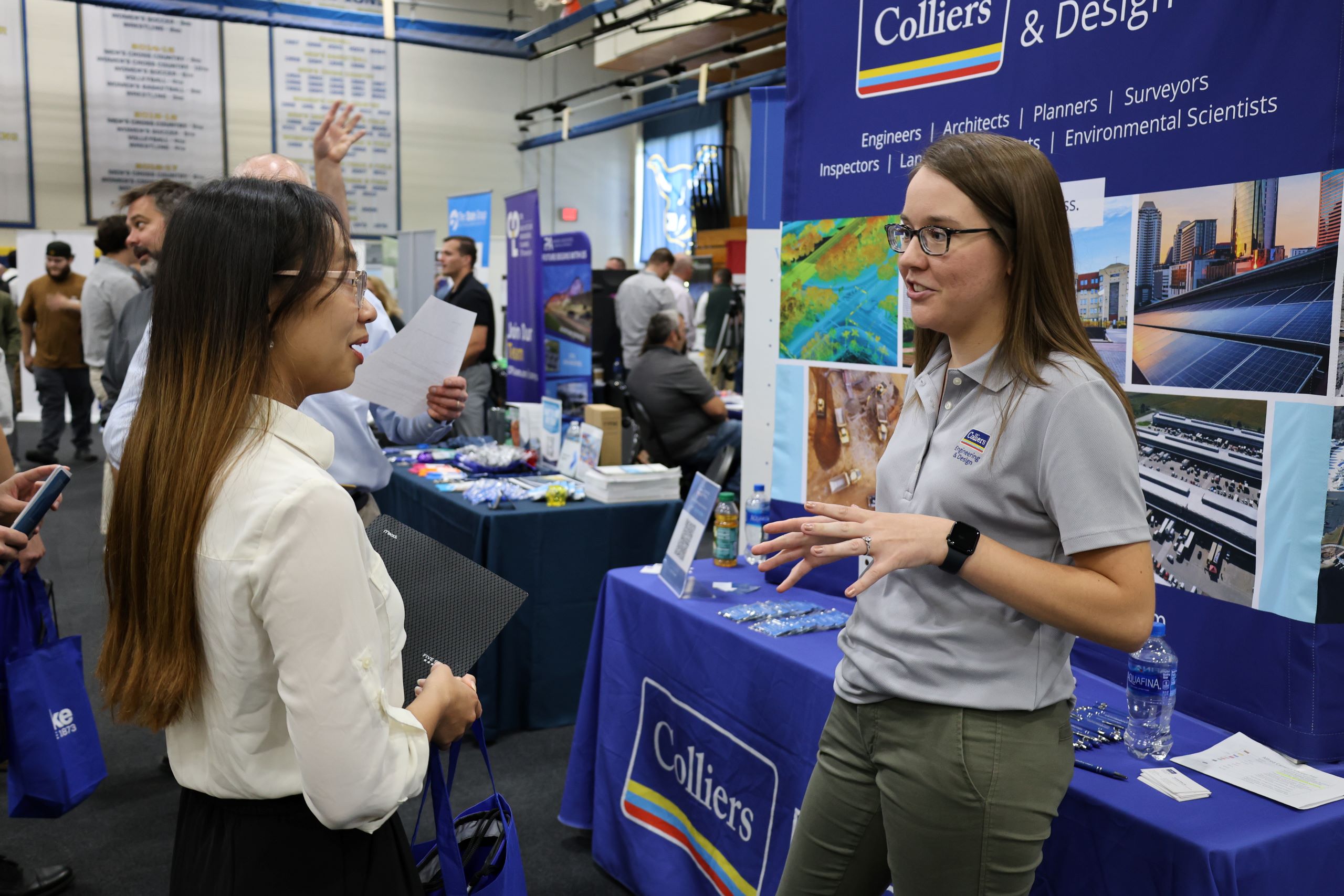 A recruiter standing in front of a booth talks to a student at a job fair at a Western New York Works college