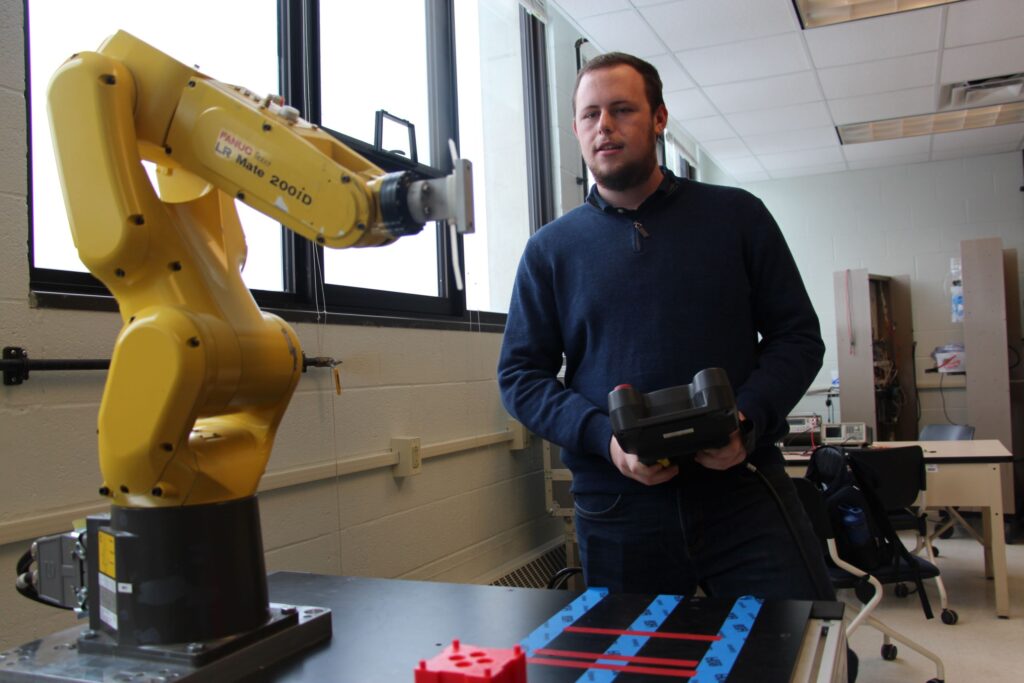 A male student practices controlling a mechanical arm in a robotics technician career training class at a Western New York Works college.