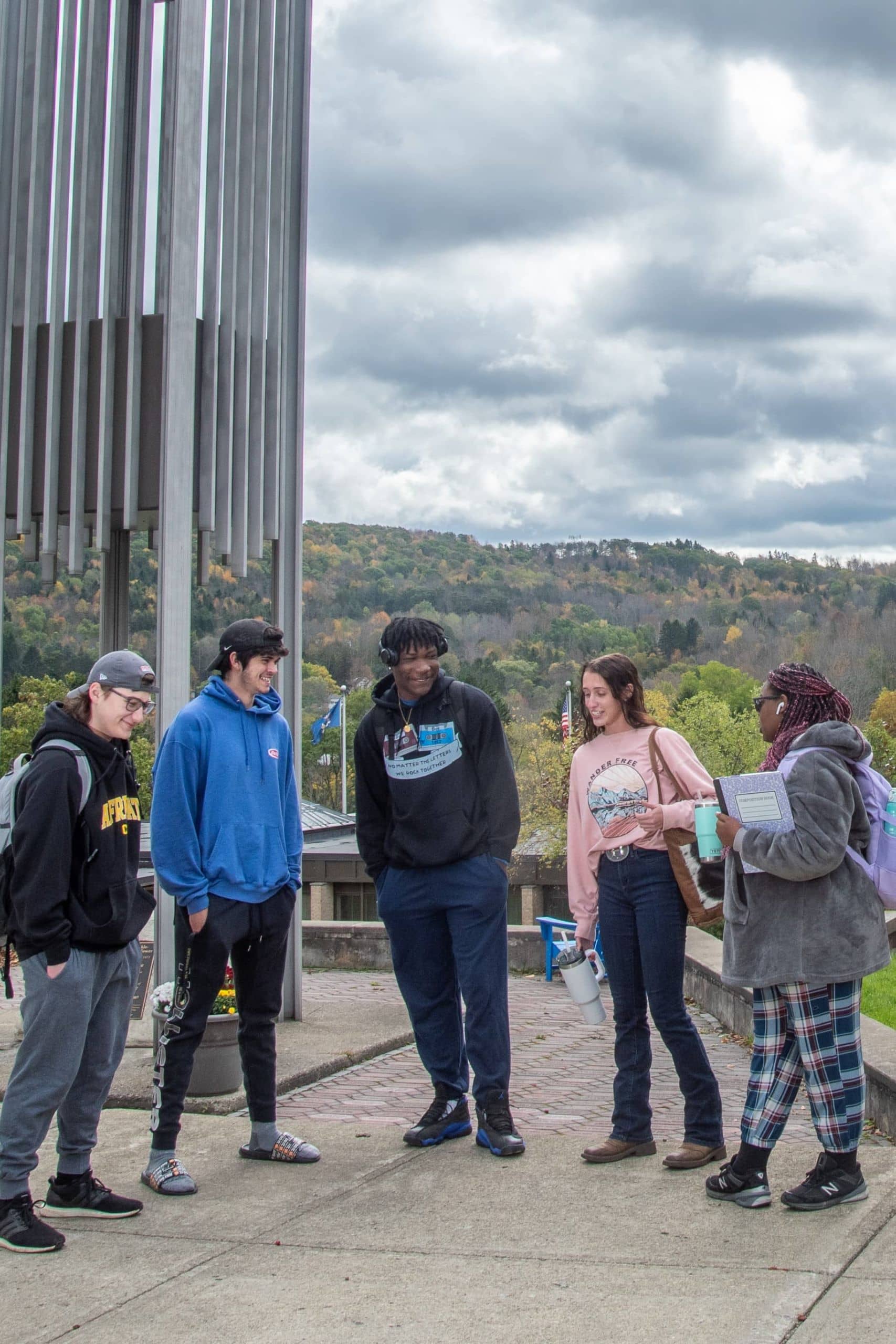 Five students gather in front of a bell tower on the Alfred State College campus.